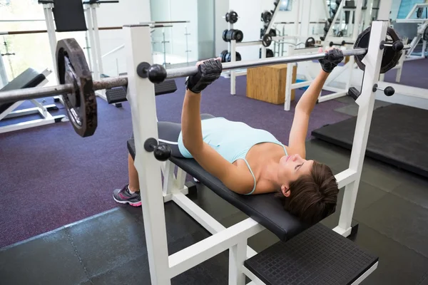 Fit brunette lifting heavy barbell lying on bench — Stock Photo, Image