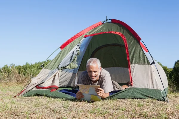 Felice camper guardando la mappa sdraiato nella sua tenda — Foto Stock