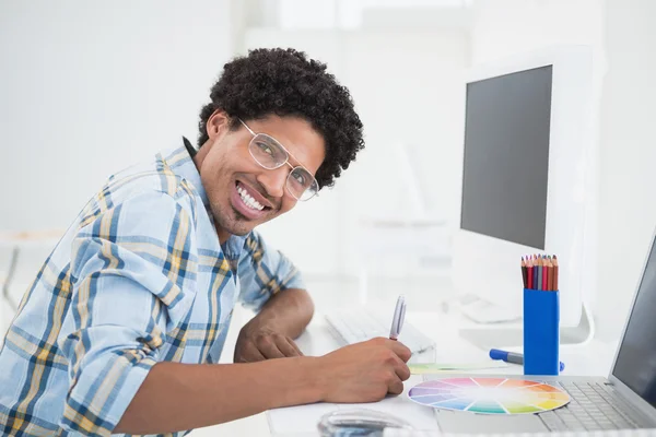 Unga formgivare arbetar vid sitt skrivbord som ler mot kameran — Stockfoto