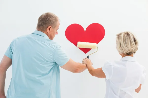 Happy older couple painting red heart — Stock Photo, Image