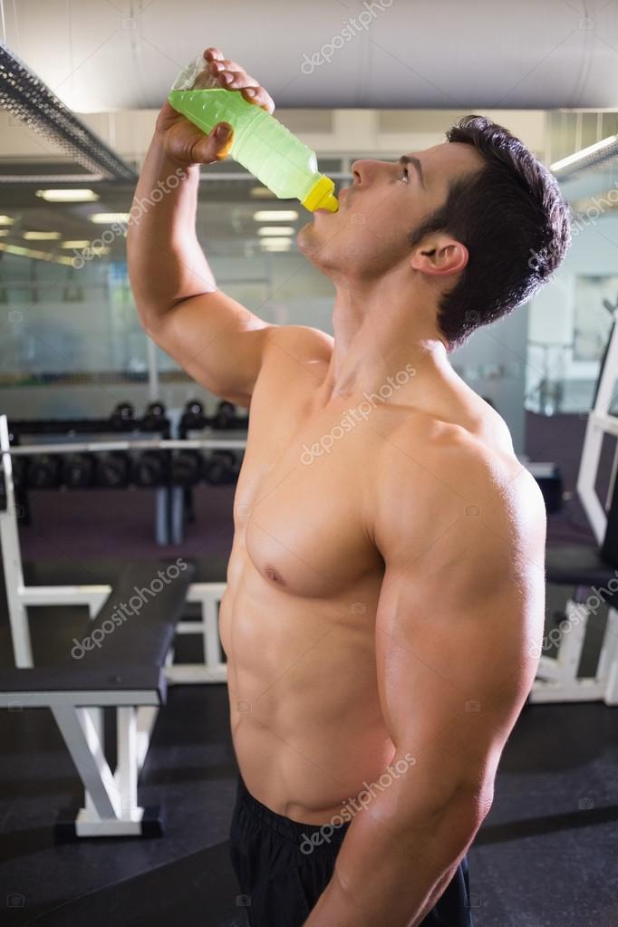 Shirtless young man drinking protein shake in gym Photograph by