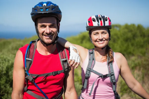 Coppia attiva in bicicletta in campagna sorridente alla fotocamera — Foto Stock