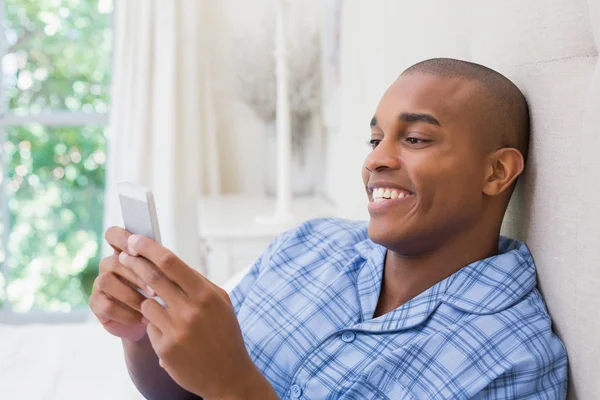 Homem feliz sentado na cama e mensagens de texto no telefone — Fotografia de Stock