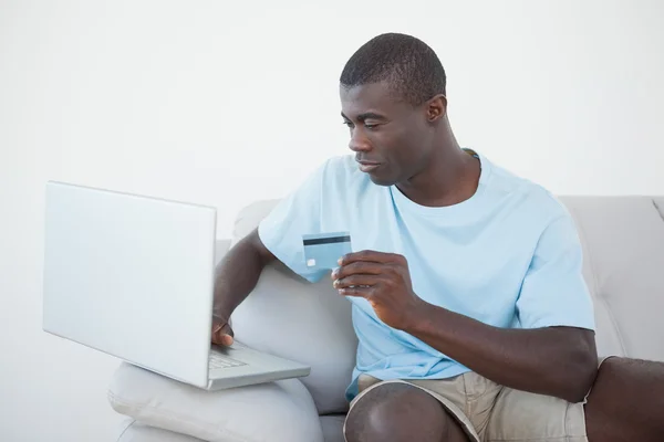 Hombre casual sentado en el sofá utilizando el ordenador portátil para comprar en línea —  Fotos de Stock