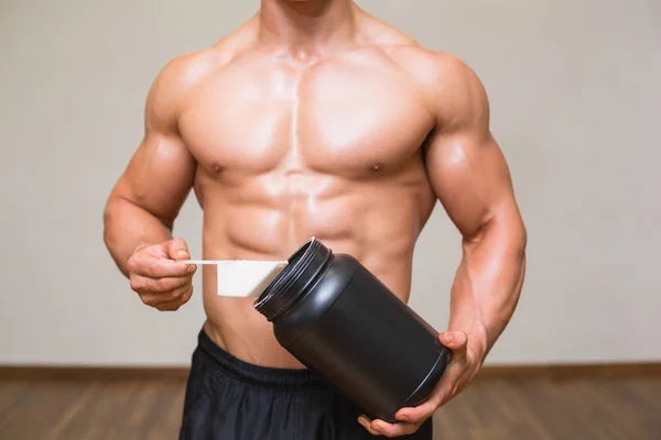 Body builder holding a scoop of protein mix in gym — Stock Photo, Image