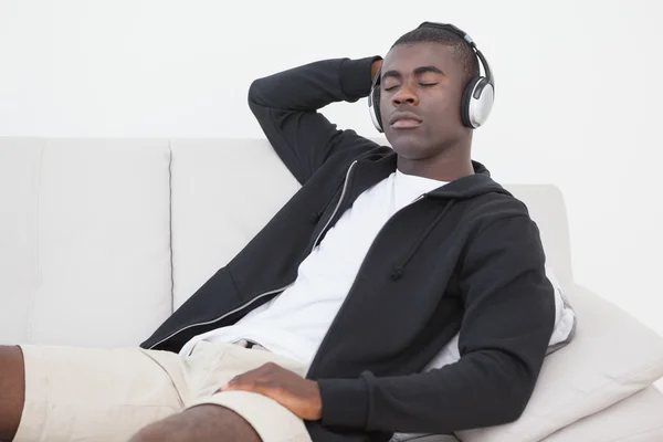 Casual homem sentado no sofá desfrutando de música com os olhos fechados — Fotografia de Stock
