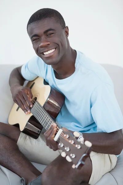 Casual man sitting on sofa playing the guitar — Stock Photo, Image