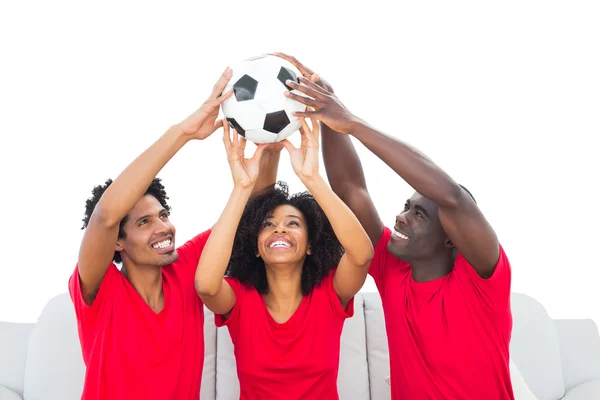 Glad fotbollsfans i röda håller upp bollen — Stockfoto