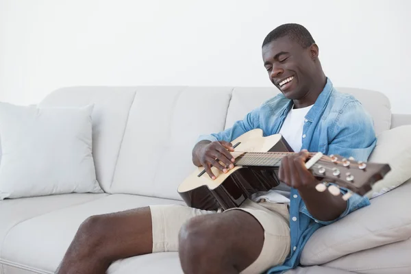 Casual man sitting on sofa playing the guitar — Stock Photo, Image