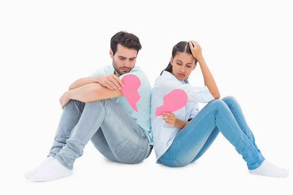 Sad couple sitting holding two halves of broken heart — Stock Photo, Image