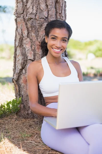 Adatta donna seduta contro l'albero utilizzando il computer portatile — Foto Stock