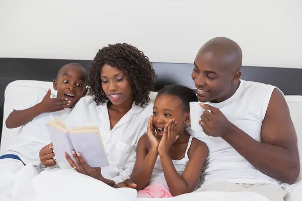 Familjen slappar tillsammans i sängen läsa bok — Stockfoto