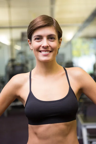 Ajuste morena em sutiã de esportes preto sorrindo para a câmera — Fotografia de Stock