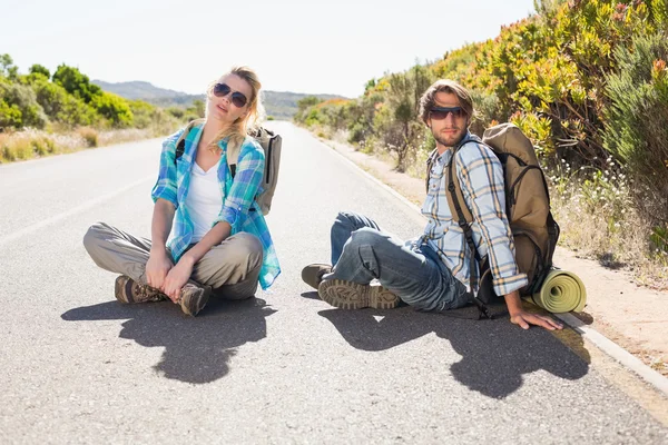 Pár sedí na silnici stopovat turistika — Stock fotografie