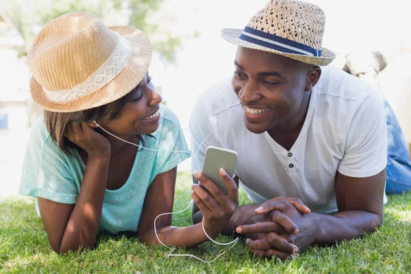 Happy couple lying in garden together listening to music — Stock Photo, Image