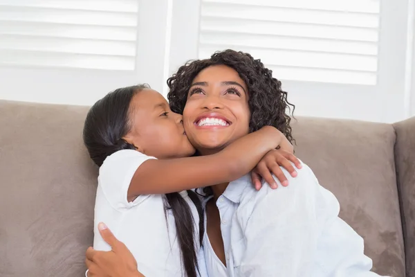 Hübsche Mutter sitzt auf der Couch, während ihre Tochter sie küsst — Stockfoto