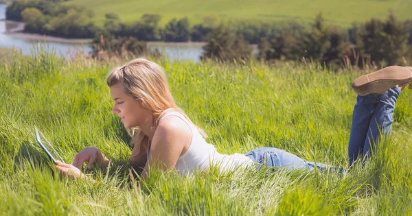 Vackra blonda liggande på gräs med hennes tablett — Stockfoto