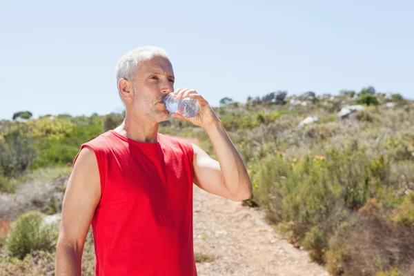 Подходящий человек пьет воду на горной тропе — стоковое фото