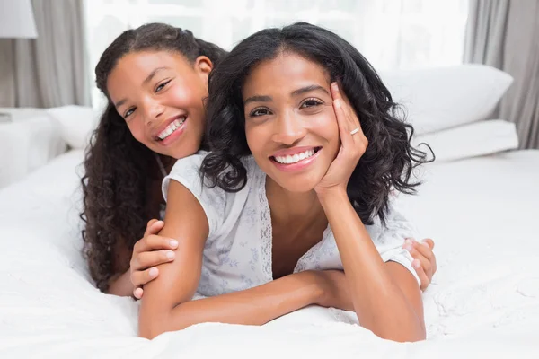 Mulher bonita deitada na cama com a filha sorrindo para a câmera — Fotografia de Stock