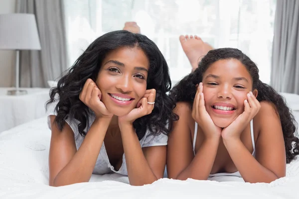 Mulher bonita deitada na cama com a filha sorrindo para a câmera — Fotografia de Stock