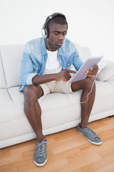 Випадковий чоловік сидить на дивані за допомогою планшетного ПК, щоб слухати музику — стокове фото