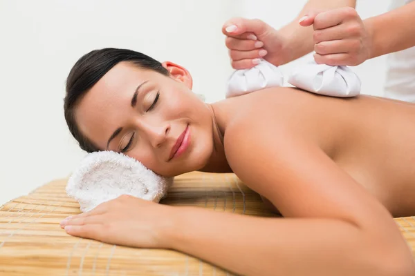 Beautiful brunette enjoying a herbal compress massage — Stock Photo, Image