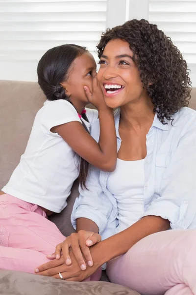 Hübsche Mutter sitzt auf der Couch und ihre Tochter flüstert — Stockfoto