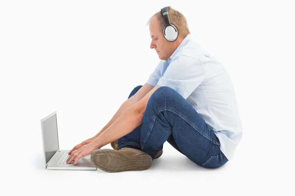 Homem maduro usando laptop ouvindo música — Fotografia de Stock