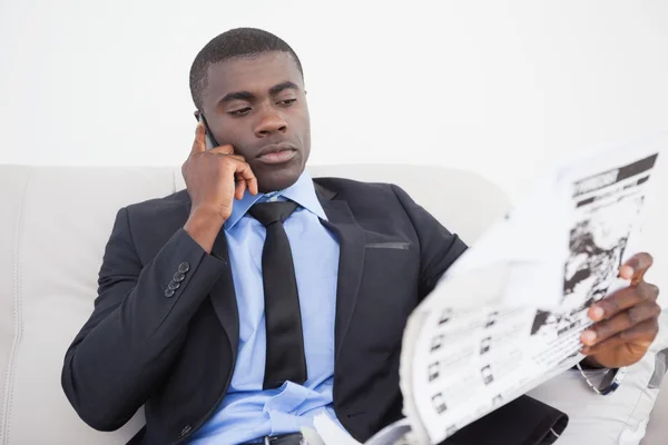 Businessman making a call while reading the paper on sofa — Stock Photo, Image