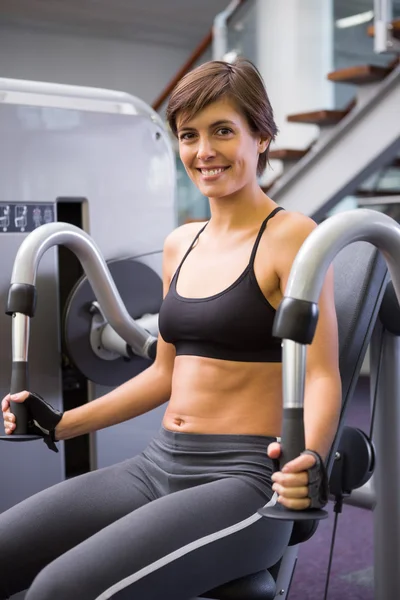 Morena sorridente usando máquina de pesos para braços — Fotografia de Stock