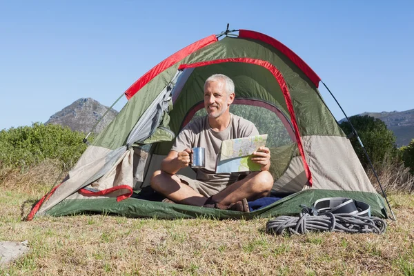 Happy camper looking at map sitting in his tent — Stock Photo, Image