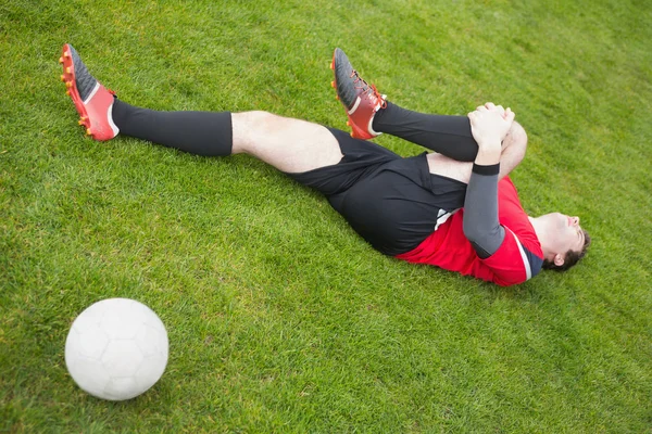 Giocatore di calcio in rosso sdraiato ferito sul campo — Foto Stock