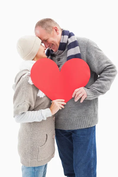 Feliz pareja madura en ropa de invierno sosteniendo el corazón rojo — Foto de Stock