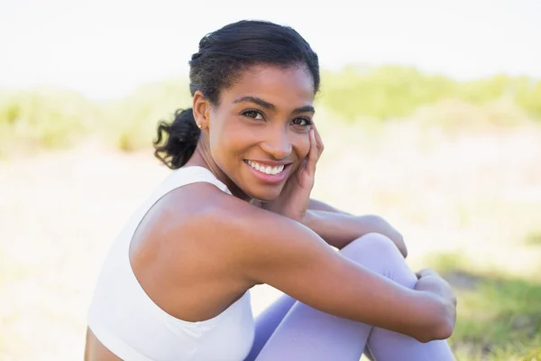 Fit mujer sentada en la hierba sonriendo a la cámara —  Fotos de Stock