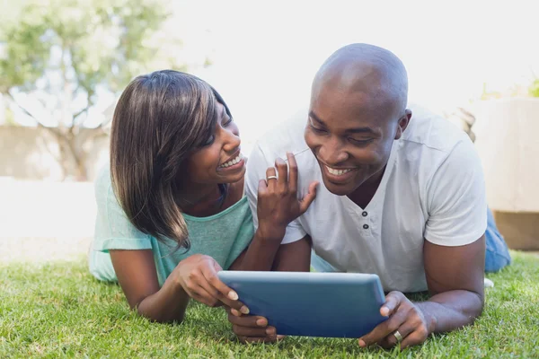 Happy couple lying in garden using tablet pc together — Stock Photo, Image