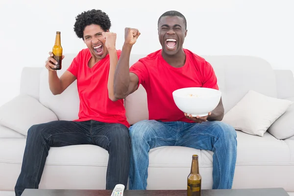 Fãs de futebol em vermelho sentados no sofá com cerveja e pipoca — Fotografia de Stock