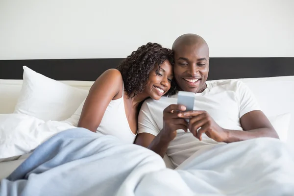 Ευτυχισμένο ζευγάρι αγκαλιά στο κρεβάτι με το smartphone — Φωτογραφία Αρχείου