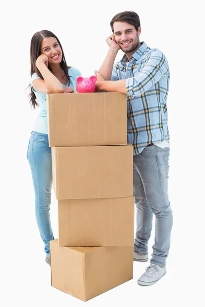 Happy young couple with moving boxes and piggy bank — Stock Photo, Image