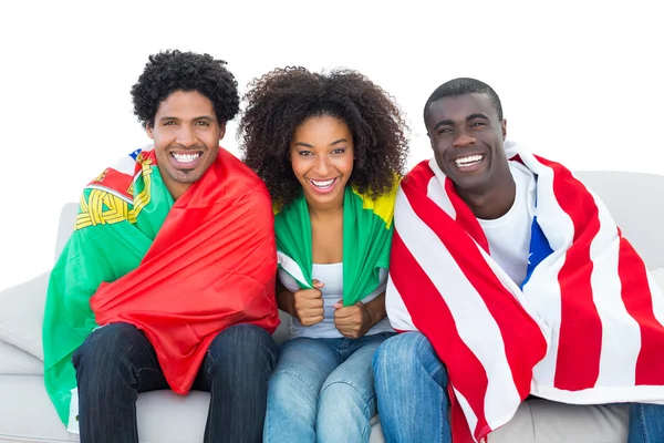 Happy football fans wrapped in flags smiling at camera — Stock Photo, Image