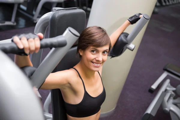 Lachende brunette met behulp van gewichten machine voor wapens — Stockfoto