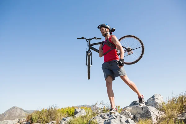 Fit ciclista che trasporta la sua moto su un terreno roccioso — Foto Stock