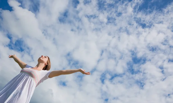 Mulher com braços estendidos contra o céu azul e nuvens — Fotografia de Stock