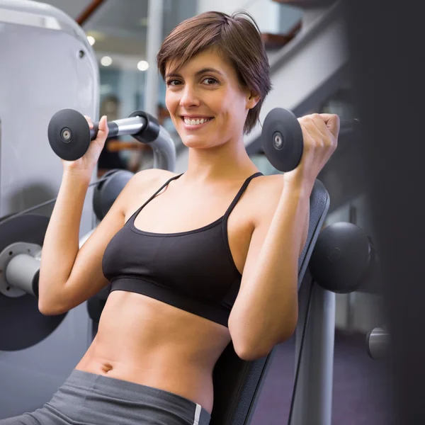 Lachende brunette met behulp van gewichten machine voor wapens — Stockfoto