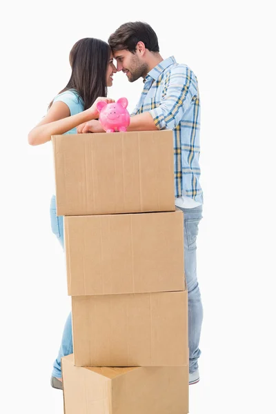 Happy young couple with moving boxes and piggy bank — Stock Photo, Image