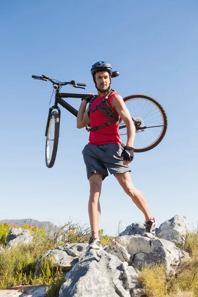 Apto ciclista carregando sua bicicleta em terreno rochoso — Fotografia de Stock