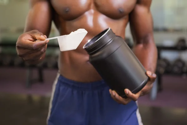 Body builder holding a scoop of protein mix in gym — Stock Photo, Image