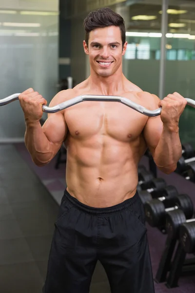 ジムでバーベルを持ち上げる筋肉の上半身裸の男の笑みを浮かべてください。 — ストック写真
