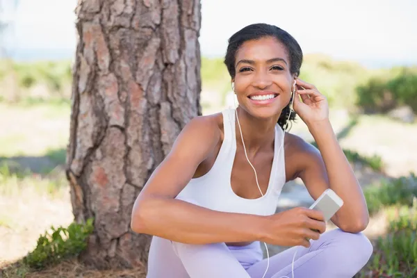 Fitte Frau sitzt gegen Baum und hört Musik — Stockfoto