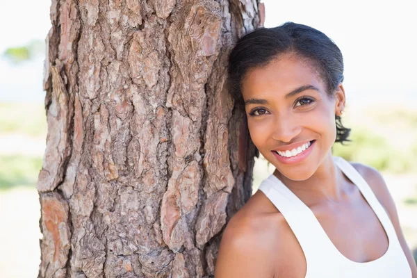 Fit mujer apoyada en el árbol sonriendo a la cámara — Foto de Stock