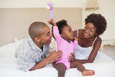 Happy parents and baby girl sitting on bed together clipart